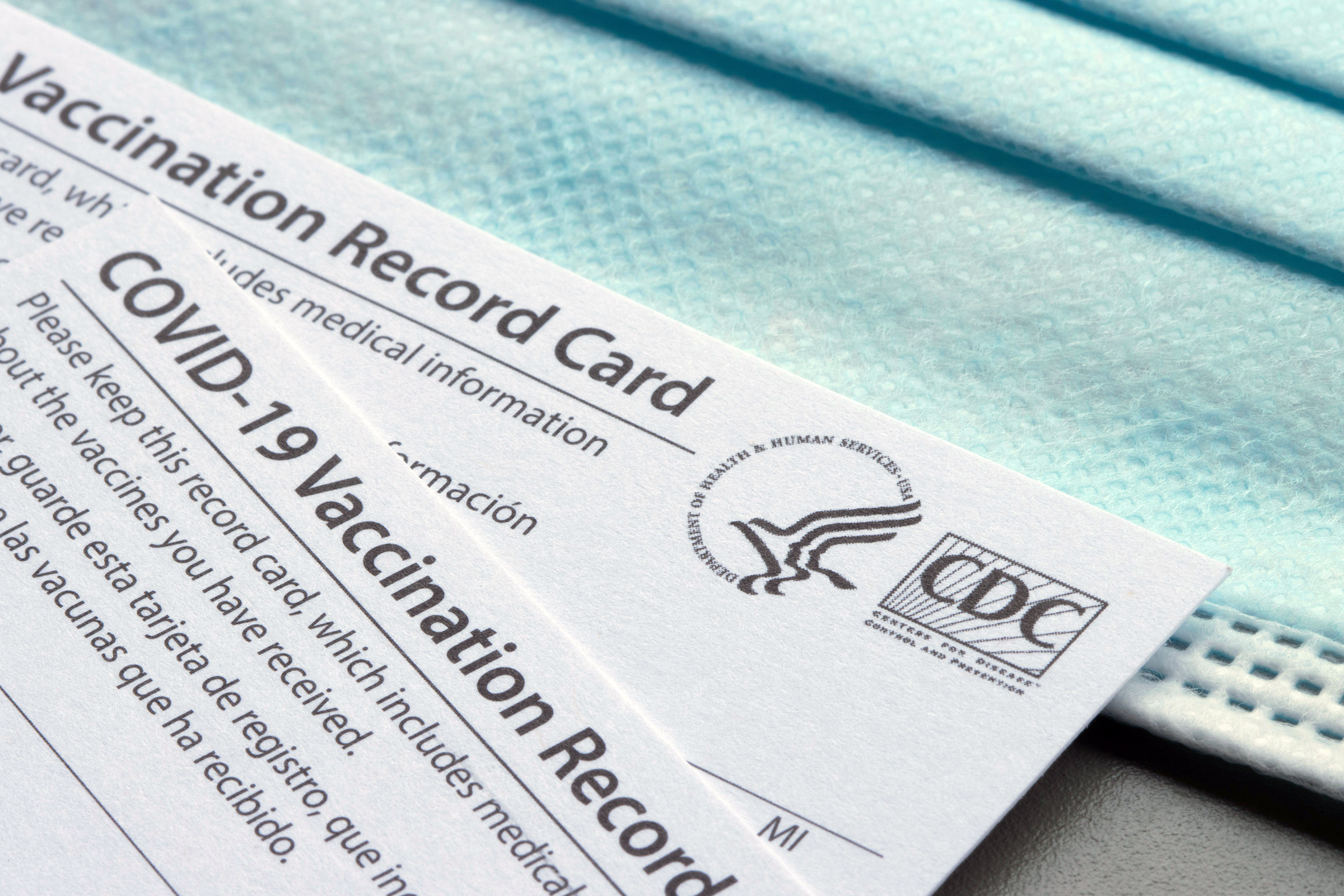 Closeup of Covid-19 Vaccination record cards issued by CDC (United States Centers for Disease Control and Prevention) on a blue disposable face mask.